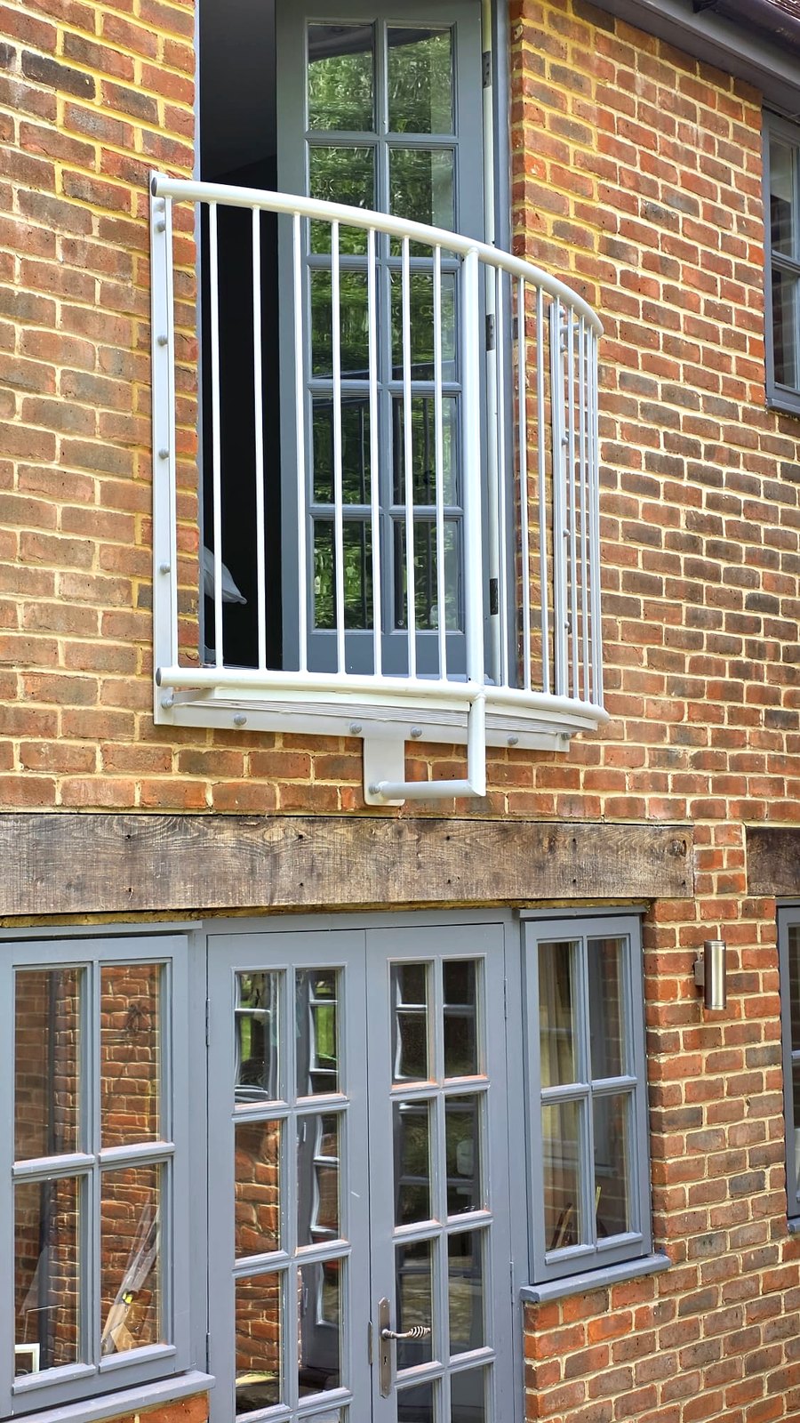 Lincoln-style curved metal Juliet balcony, powder-coated light grey, on a brick house